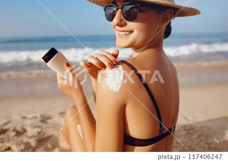 Beautiful Woman in Bikini Applying Sun Cream on Tanned  Shoulder. Sun Protection. Skin and Body Care. Girl Using Sunscreen to Skin. Portrait Of Female Holding Suntan Lotion and Moisturizing Sunblock. 137406247