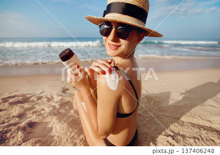Woman applying sun cream on tanned shoulder. Skincare. Body Sun protection suncream. Bikini hat woman using moisturizing sunscreen lotion on back Woman applying sun cream on tanned shoulder. Skincare. Body Sun protection suncream. Bikini hat woman using moisturizing sunscreen lotion on back 137406248
