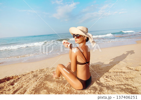 Beautiful Woman in Bikini Applying Sun Cream on Tanned Shoulder. Sun Protection. Skin and Body Care. Girl Using Sunscreen to Skin. Portrait Of Female Holding Suntan Lotion and Moisturizing Sunblock. Beautiful Woman in Bikini Applying Sun Cream on Tanned Shoulder. Sun Protection. Skin and Body Care. Girl Using Sunscreen to Skin. Portrait Of Female Holding Suntan Lotion and Moisturizing Sunblock. 137406251