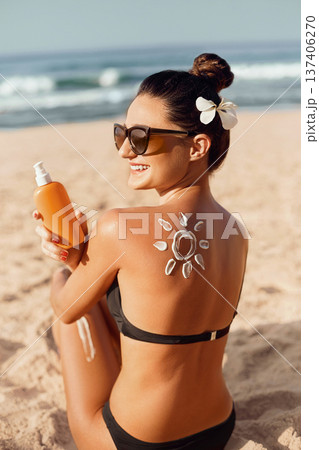 Beauty Woman Applying Sun Cream  on Tanned  Shoulder In Form Of The Sun. Sun Protection.Sun Cream. Skin and Body Care. Girl Using Sunscreen to Skin. Female Holding Suntan Lotion and Moisturizing 137406270