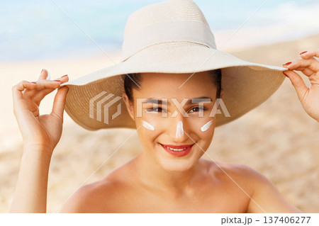 Beauty Woman smile applying sun cream on face. Skin care. Body Sun protection. sunscreen. Female in hat smear moisturizing lotion on skin Beauty Woman smile applying sun cream on face. Skin care. Body Sun protection. sunscreen. Female in hat smear moisturizing lotion on skin 137406277