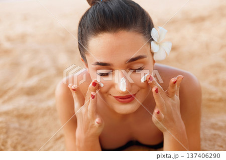 Beautiful happy cute woman applying suntan cream to her nose on the beach. Body Sun protection. Sunscreen. Bikini woman smear moisturizing lotion on skin.Suntan Beautiful happy cute woman applying suntan cream to her nose on the beach. Body Sun protection. Sunscreen. Bikini woman smear moisturizing lotion on skin.Suntan 137406290