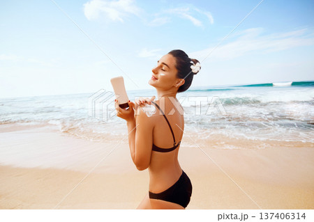 Woman applying sunscreen creme on tanned shoulder. Skincare. Body Sun protection sun cream. Bikini woman smear moisturizing lotion on back Woman applying sunscreen creme on tanned shoulder. Skincare. Body Sun protection sun cream. Bikini woman smear moisturizing lotion on back 137406314
