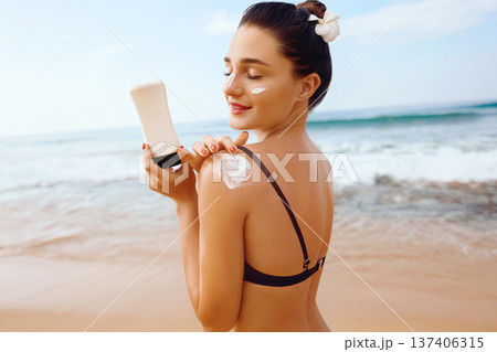 Beautiful woman in bikini applying sun cream on tanned shoulder. Sun protection. Skin and body care. Girl using sunscreen to skin. Portrait of female holding Suntan lotion and moisturizing sunblock. Beautiful woman in bikini applying sun cream on tanned shoulder. Sun protection. Skin and body care. Girl using sunscreen to skin. Portrait of female holding Suntan lotion and moisturizing sunblock. 137406315