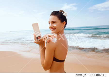Woman putting sunblock lotion on shoulder before tanning during summer holiday on beach vacation resort 137406318