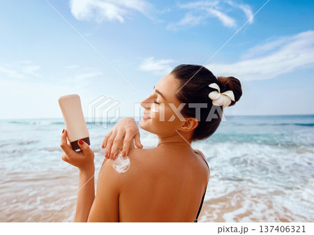 Beauty Woman apply Sun cream on tanned  back. Skin and Body Care. Sun protection. Portrait of Female in Bikini applying moisturizing sunscreen lotion and Sunblock. Girl Holding Suntan Lotion. 137406321