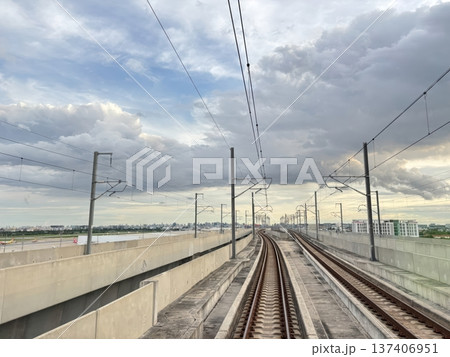 Modern elevated train tracks curving towards a cityscape under dramatic sky Modern elevated train tracks curving towards a cityscape under dramatic sky 137406951
