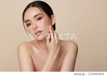 A beautiful young Asian woman with clean, fresh skin against a beige background. Skincare, facial treatment, cosmetology, beauty, and spa. An elegant portrait of an Asian woman. 137407001