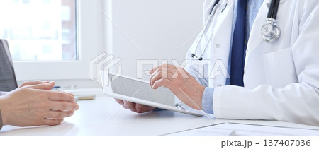 Close-up of doctor man showing information on tablet to patient woman during medical visit, explaining diagnosis and treatment options, providing medical consultation. Medicine concept Close-up of doctor man showing information on tablet to patient woman during medical visit, explaining diagnosis and treatment options, providing medical consultation. Medicine concept 137407036
