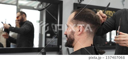 Skilled barber working on male client's hairstyle, carefully combing and preparing precision cut in contemporary barbershop setting 137407068