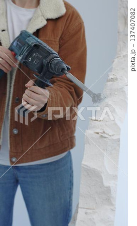 Unknown female construction worker demolishing concrete wall with rotary hammer, wearing protective safety gear. Renovation concept, closeup vertical view Unknown female construction worker demolishing concrete wall with rotary hammer, wearing protective safety gear. Renovation concept, closeup vertical view 137407082
