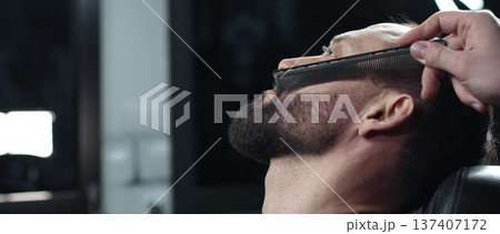 Skilled barber carefully combing thick beard of male client, providing professional grooming service in traditional barbershop setting with precision and attention to detail 137407172