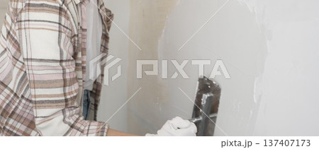 Unknown female construction worker wearing protective gloves applying plaster, smoothing wall surface during home renovation work 137407173