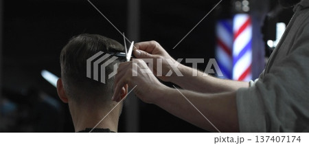 Professional barber trimming client's hair with precision scissors, creating polished hairstyle in contemporary grooming space 137407174