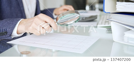 Auditor analyzing financial data with magnifying glass, scrutinizing business documents and accounting reports in office. Audit and taxes in business Auditor analyzing financial data with magnifying glass, scrutinizing business documents and accounting reports in office. Audit and taxes in business 137407200