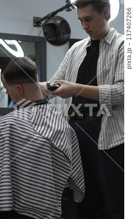 Professional barber carefully trimming customer's hair with electric clipper, providing a stylish and precise haircut in a modern barbershop environment 137407266