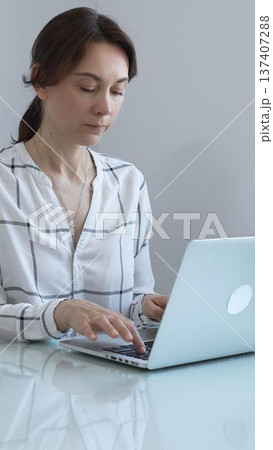 Professional businesswoman working on laptop, sitting at glass desk in bright contemporary workspace, embodying corporate success and concentration. Business people concept. Professional businesswoman working on laptop, sitting at glass desk in bright contemporary workspace, embodying corporate success and concentration. Business people concept. 137407288