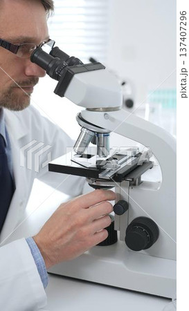 Medical scientist wearing glasses using microscope analyzing samples in modern laboratory doing scientific research. Medicine, health care and science concept Medical scientist wearing glasses using microscope analyzing samples in modern laboratory doing scientific research. Medicine, health care and science concept 137407296