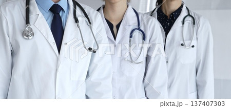 Medical team standing together, doctors and healthcare professionals wearing white lab coats and stethoscopes, symbolizing partnership and expertise in modern clinic or hospital environment 137407303