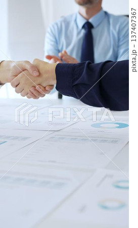 Business woman partners are shaking hands in office with financial charts, laptop and reports on table, symbolizing success, teamwork and agreement. Handshake concept 137407367