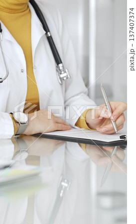 Female physician or medic completing paperwork, preparing a diagnosis, or providing healthcare service in a clean modern office. Medicine, healthcare and science concept 137407374