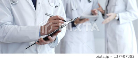 Doctor writing on a clipboard during a medical team discussion, collaborating on patient care, documentation, and healthcare strategy in a clinical setting 137407382