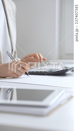 Businesswoman is calculating annual tax using calculator and taking notes in the office, managing domestic budget and checking financial documents. Audit and taxes in business Businesswoman is calculating annual tax using calculator and taking notes in the office, managing domestic budget and checking financial documents. Audit and taxes in business 137407385