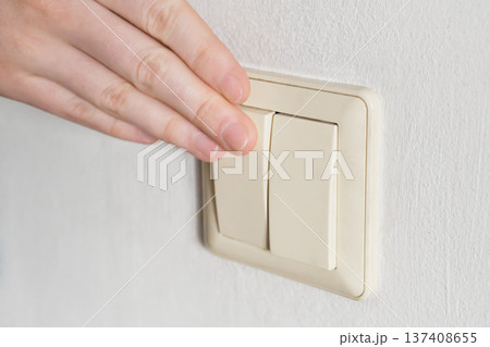 Hand pressing light switch on white wall, controlling power 137408655
