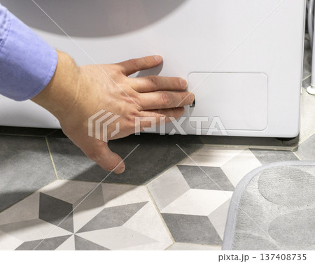 Man opening the drain pump filter access panel of the front loading washing machine Man opening the drain pump filter access panel of the front loading washing machine 137408735