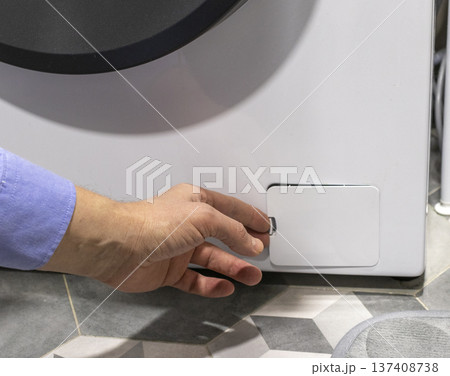 Man opening the drain pump filter access panel of the front loading washing machine Man opening the drain pump filter access panel of the front loading washing machine 137408738
