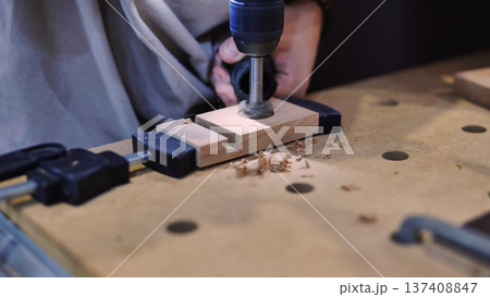Woodworking project in progress, drilling a hole into wooden workpiece fixed with clamps Woodworking project in progress, drilling a hole into wooden workpiece fixed with clamps 137408847