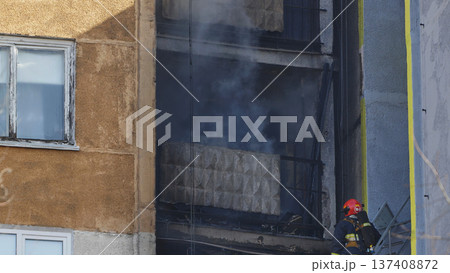 Firefighter checking burning building during an apartment fire, smoke coming from windows Firefighter checking burning building during an apartment fire, smoke coming from windows 137408872