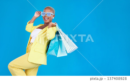 Fashion, sale and black woman with shopping, bag and glasses in studio excited and smile on blue background. Retail, store and African female customer happy with boutique, discount and mall deal 137408928