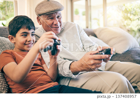 Family, fun and a boy gaming with his grandfather on a sofa in the living room of their home during a visit. Video game, children and a senior man learning how to play from his gamer grandson Family, fun and a boy gaming with his grandfather on a sofa in the living room of their home during a visit. Video game, children and a senior man learning how to play from his gamer grandson 137408957