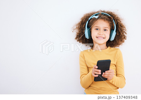Girl kid, portrait and smartphone, headphones and music with smile isolated on white background. Technology, audio streaming and social media, mockup space and child, mobile app and radio in studio 137409348