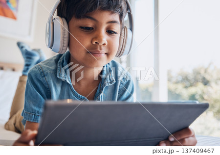 Boy kid, tablet and headphones on bed, reading or idea with e learninng, movie and relax with web video. Male child, digital touchscreen and thinking in bedroom for audio, show and streaming in home Boy kid, tablet and headphones on bed, reading or idea with e learninng, movie and relax with web video. Male child, digital touchscreen and thinking in bedroom for audio, show and streaming in home 137409467