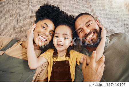 Portrait, family and a boy with his parents on the floor of the living room in their home together from above. Face, smile or love with an interracial mother, father and son lying down closeup 137410105