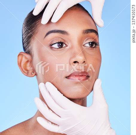 Skincare, doctor and face of Indian woman for plastic surgery, cosmetics and facial treatment in studio. Dermatology, consulting and hands person for anti aging, collagen or beauty on blue background 137410173
