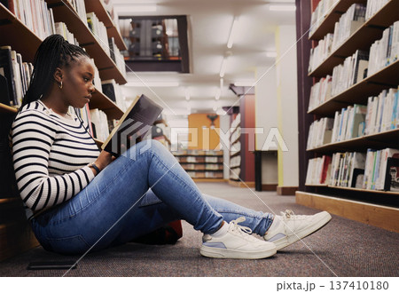Research, book and a black woman in a library for reading, college knowledge or studying on the floor. Scholarship, student and an African girl at a university or a bookshop for education or learning 137410180