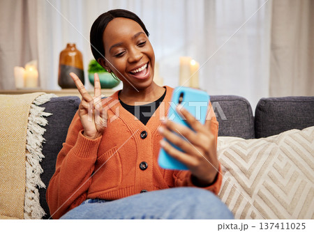 Selfie, black woman and peace sign at home with a smile for social media, motivation and video call. Photo, happy and African female person in a living room with a v and emoji hand gesture at house Selfie, black woman and peace sign at home with a smile for social media, motivation and video call. Photo, happy and African female person in a living room with a v and emoji hand gesture at house 137411025