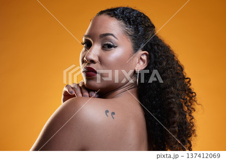 Beauty, portrait and a woman with a tattoo in studio for cosmetics, makeup and dermatology. Closeup of a young female model on an orange background in studio with body art, confidence and skin glow Beauty, portrait and a woman with a tattoo in studio for cosmetics, makeup and dermatology. Closeup of a young female model on an orange background in studio with body art, confidence and skin glow 137412069