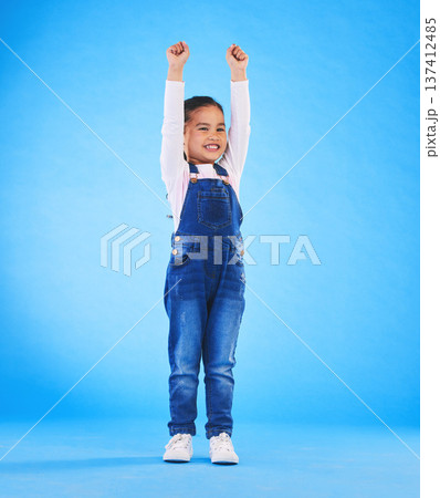 Celebration, girl child and champion, winner and achievement with happiness and excited isolated on blue background. Cheers, yes and winning with success, pride and happy kid with arms up in a studio 137412485