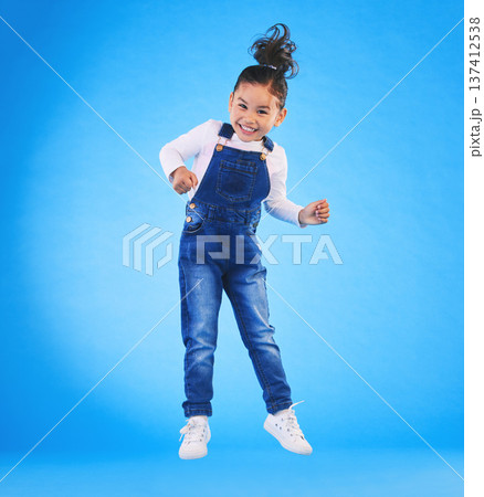 Happy, jumping and portrait of a child in a studio with excitement, joy or wow expression. Happiness, smile and full length of a girl kid model moving for good news isolated by a blue background. Happy, jumping and portrait of a child in a studio with excitement, joy or wow expression. Happiness, smile and full length of a girl kid model moving for good news isolated by a blue background. 137412538
