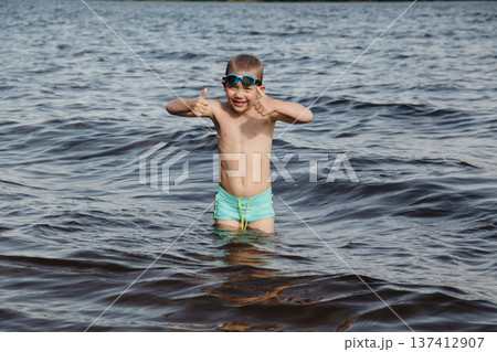 child happily excitedly enters water, swims, dives lake or pond on a hot, sunny summer day during vacation or school break. active healthy lifestyle. child wearing turquoise swimming trunks goggles. child happily excitedly enters water, swims, dives lake or pond on a hot, sunny summer day during vacation or school break. active healthy lifestyle. child wearing turquoise swimming trunks goggles. 137412907