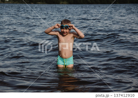 child happily excitedly enters water, swims, dives lake or pond on a hot, sunny summer day during vacation or school break. active healthy lifestyle. child wearing turquoise swimming trunks goggles. child happily excitedly enters water, swims, dives lake or pond on a hot, sunny summer day during vacation or school break. active healthy lifestyle. child wearing turquoise swimming trunks goggles. 137412910