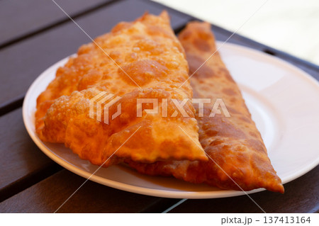 Hearty lunch: Chebureks with meat on a white plate on a wooden table. Big chebureks for dinner. Meat pies. Close-up. Hearty lunch: Chebureks with meat on a white plate on a wooden table. Big chebureks for dinner. Meat pies. Close-up. 137413164