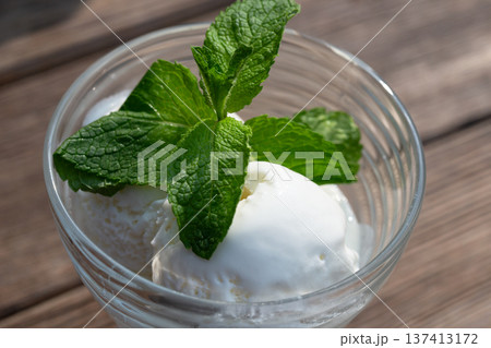 Delicious butter ice cream in a glass bowl with green mint on a wooden board, close-up. Delicious butter ice cream in a glass bowl with green mint on a wooden board, close-up. 137413172
