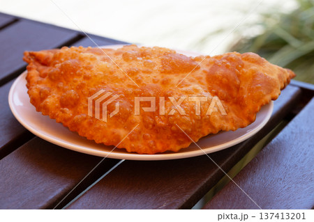 Hearty lunch: Chebureks with meat on a white plate on a wooden table. Big chebureks for dinner. Meat pies. Close-up. Hearty lunch: Chebureks with meat on a white plate on a wooden table. Big chebureks for dinner. Meat pies. Close-up. 137413201