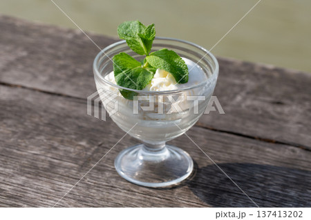 Delicious butter ice cream in a glass bowl with green mint on a wooden board, close-up. Delicious butter ice cream in a glass bowl with green mint on a wooden board, close-up. 137413202