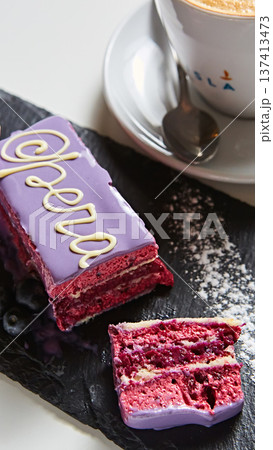 Opera cake slice with vibrant purple glaze, delicate white chocolate calligraphy 137413473
